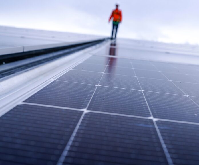Engineer,In,Safety,Gear,Standing,On,Large,Solar,Panel,Rooftop,